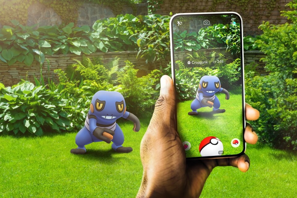 A Pokémon GO promotional image, showing a player's encounter with a Croagunk who also appears outside of the phone screen in the real world.